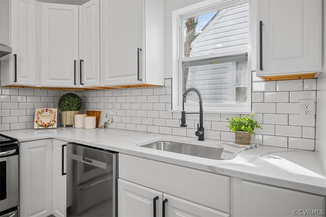 Kitchen featuring backsplash, appliances with stainless steel finishes, white cabinetry, and light stone counters