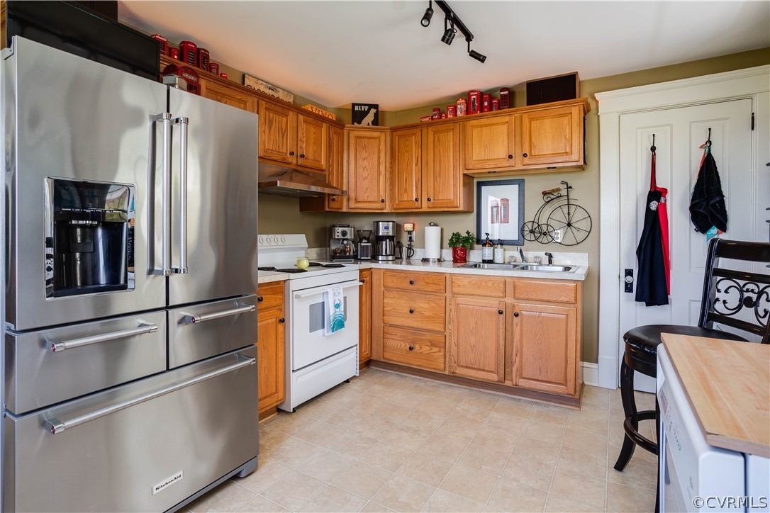 Kitchen featuring high end refrigerator, electric stove, rail lighting, sink, and light tile floors