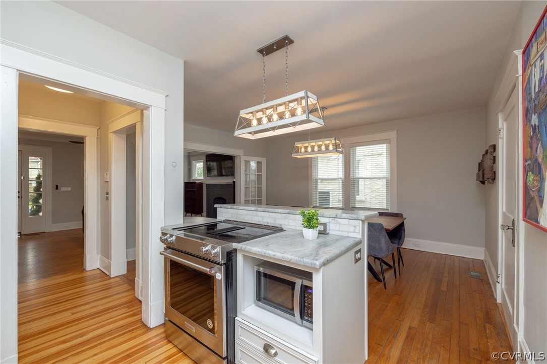 Kitchen with appliances with stainless steel finishes, light hardwood / wood-style floors, decorative light fixtures, and light stone counters