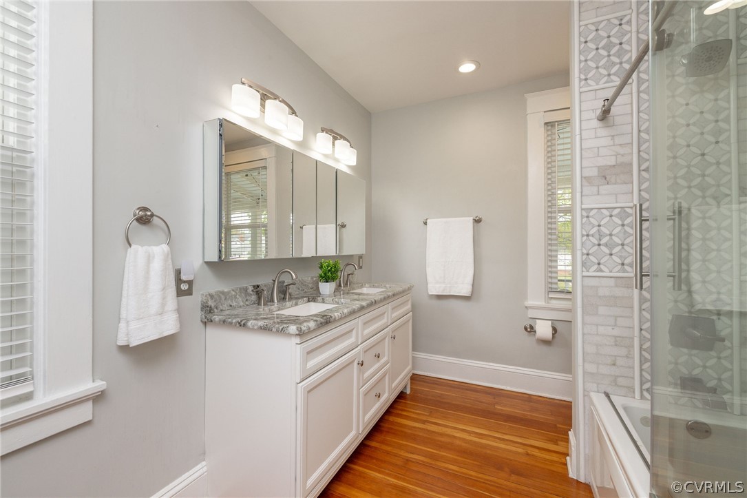 Bathroom featuring hardwood / wood-style floors, combined bath / shower with glass door, dual vanity, and a wealth of natural light