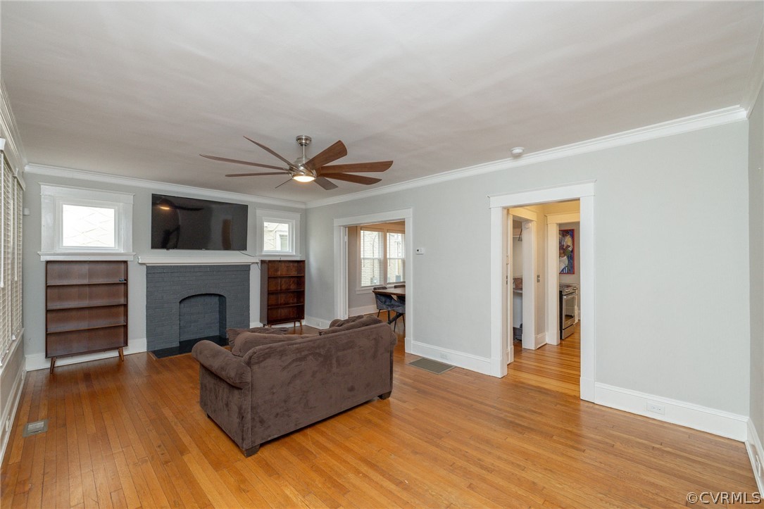 Living room with ornamental molding, light hardwood / wood-style flooring, a brick fireplace, and plenty of natural light