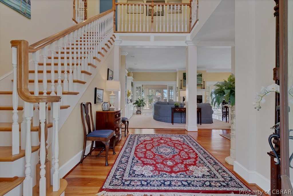 Foyer entrance featuring crown molding, light hardwood / wood-style floors, decorative columns, and a high ceiling