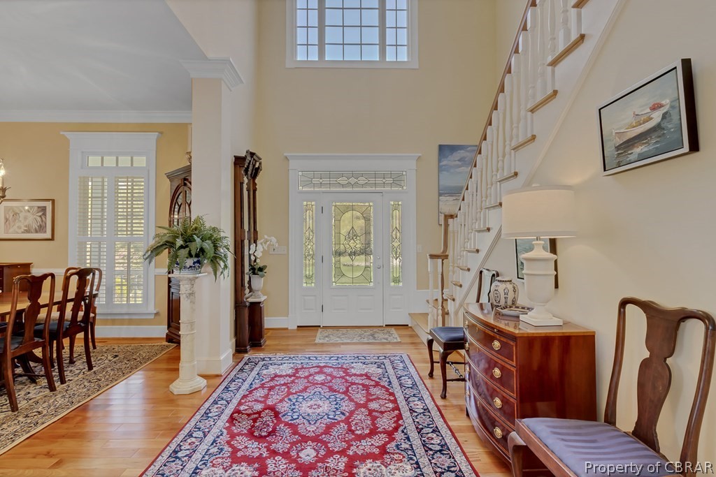 Entryway featuring ornate columns, crown molding, light wood-type flooring, and a high ceiling