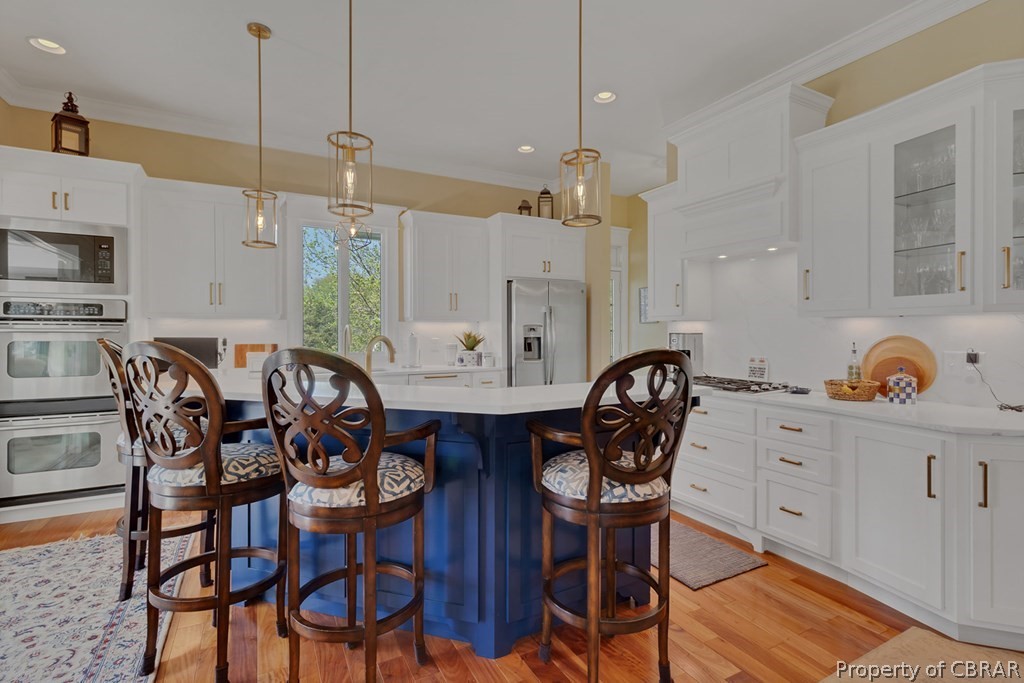 Kitchen featuring decorative light fixtures, light hardwood / wood-style flooring, white cabinets, and stainless steel appliances