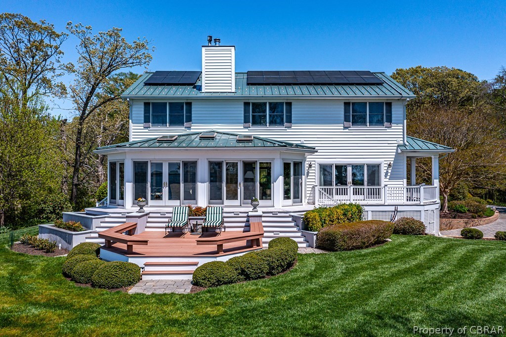 Rear view of property featuring a wooden deck, a lawn, solar panels, and a sunroom
