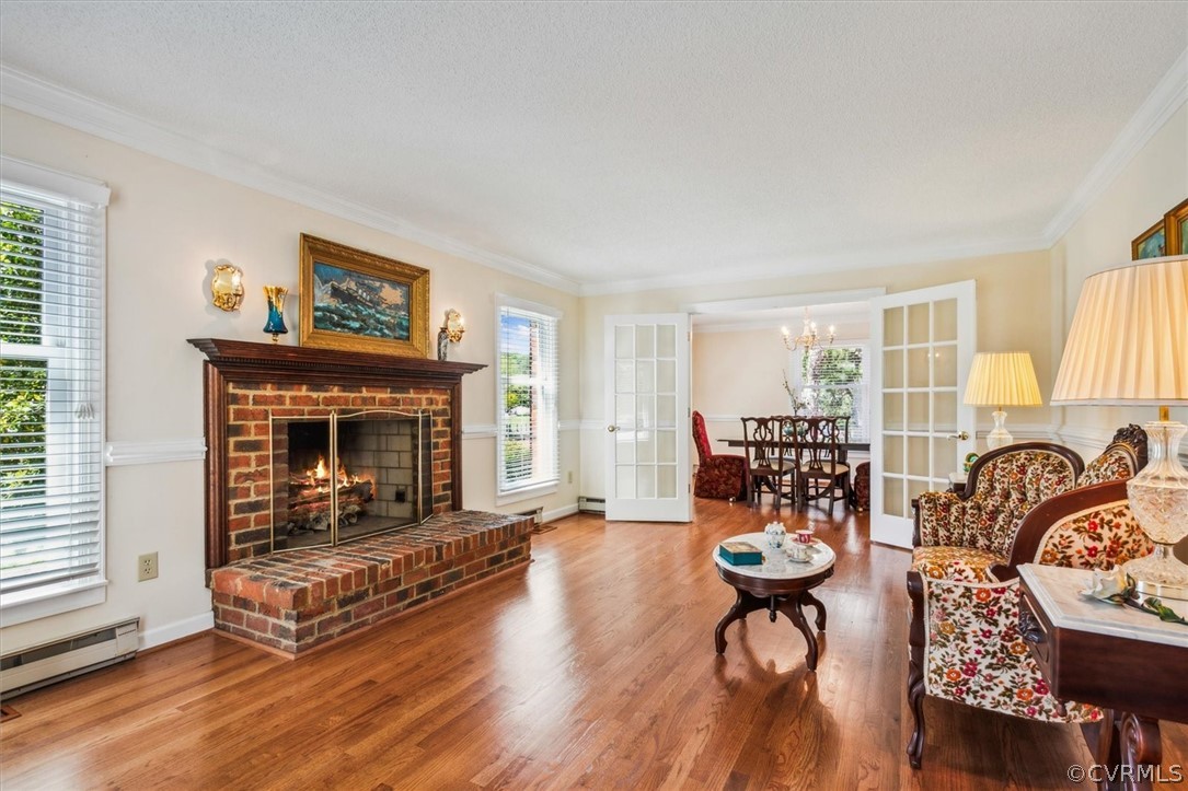 Living room featuring a brick fireplace, hardwood / wood-style flooring, baseboard heating, a chandelier, and ornamental molding