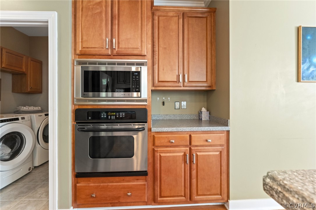 Kitchen with appliances with stainless steel finishes, washing machine and clothes dryer, and light tile floors