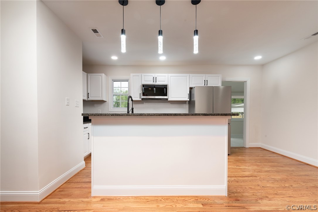 Kitchen featuring light hardwood / wood-style flooring, stainless steel appliances, white cabinets, and hanging light fixtures