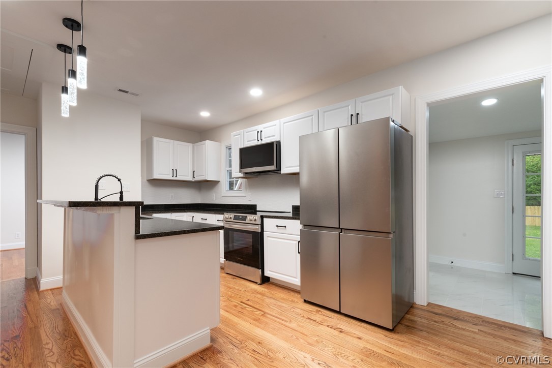 Kitchen featuring white cabinets, hanging light fixtures, light tile flooring, and stainless steel appliances