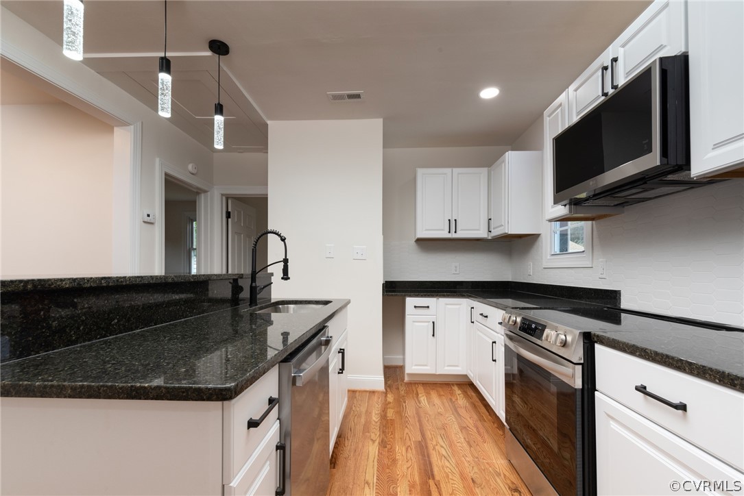 Kitchen featuring appliances with stainless steel finishes, hanging light fixtures, white cabinets, and sink