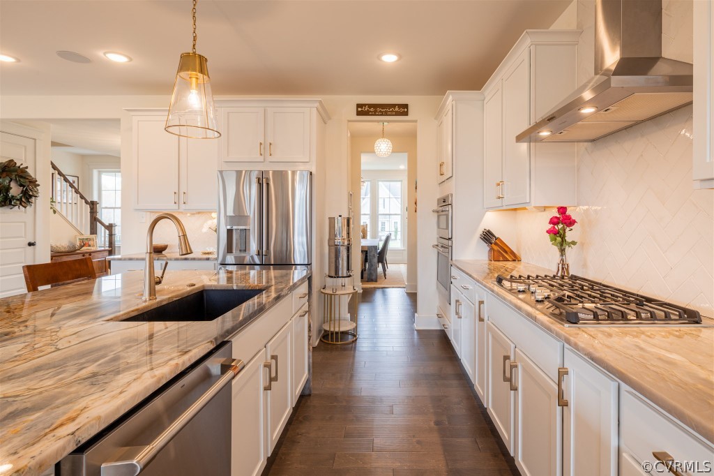 Kitchen with wall chimney exhaust hood, a healthy amount of sunlight, pendant lighting, and stainless steel appliances