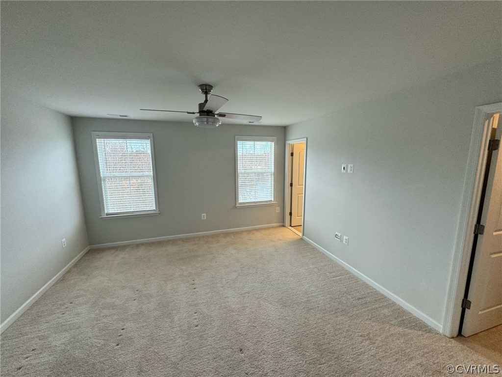 Spare room featuring light colored carpet, ceiling fan, and a healthy amount of sunlight