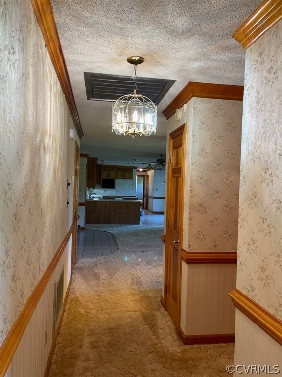 Corridor with ornamental molding, light carpet, a textured ceiling, and a chandelier