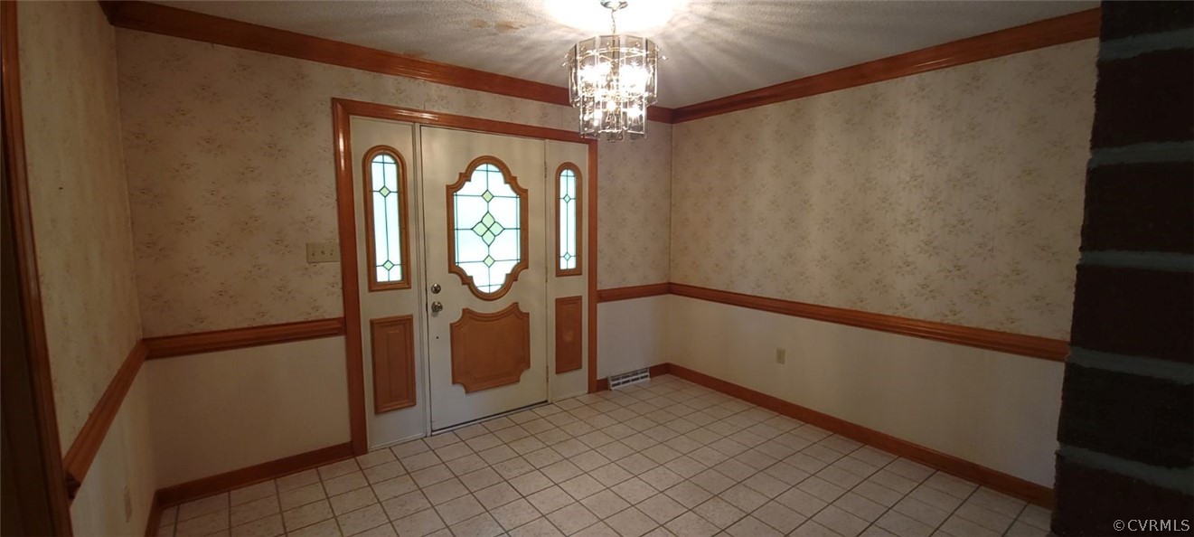 Tiled entrance foyer featuring crown molding and an inviting chandelier