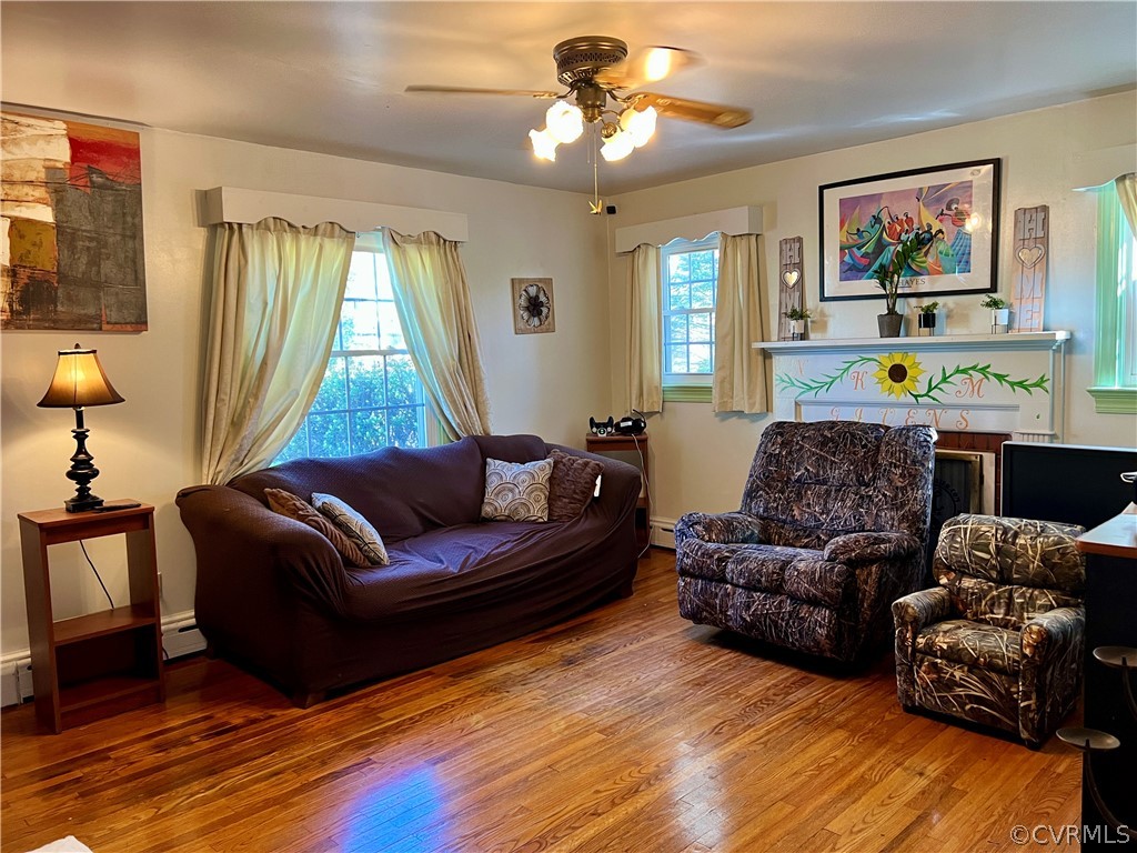 Living room featuring wood-type flooring, ceiling fan, and a baseboard heating unit