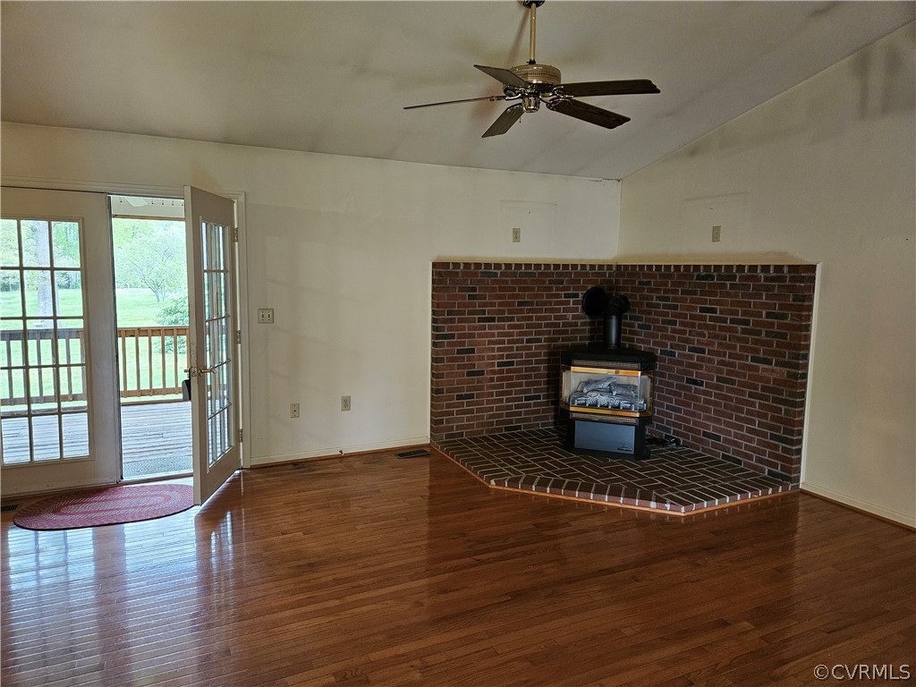 Unfurnished living room featuring lofted ceiling, a wood stove, ceiling fan, and hardwood / wood-style flooring