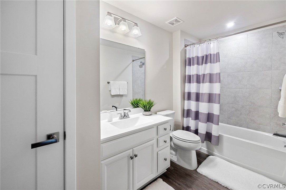 Full bathroom with hardwood / wood-style floors, toilet, shower / bathtub combination with curtain, and large vanity