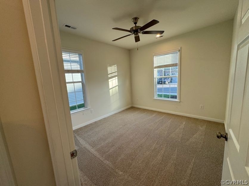 Unfurnished room with ceiling fan, carpet flooring, and a wealth of natural light