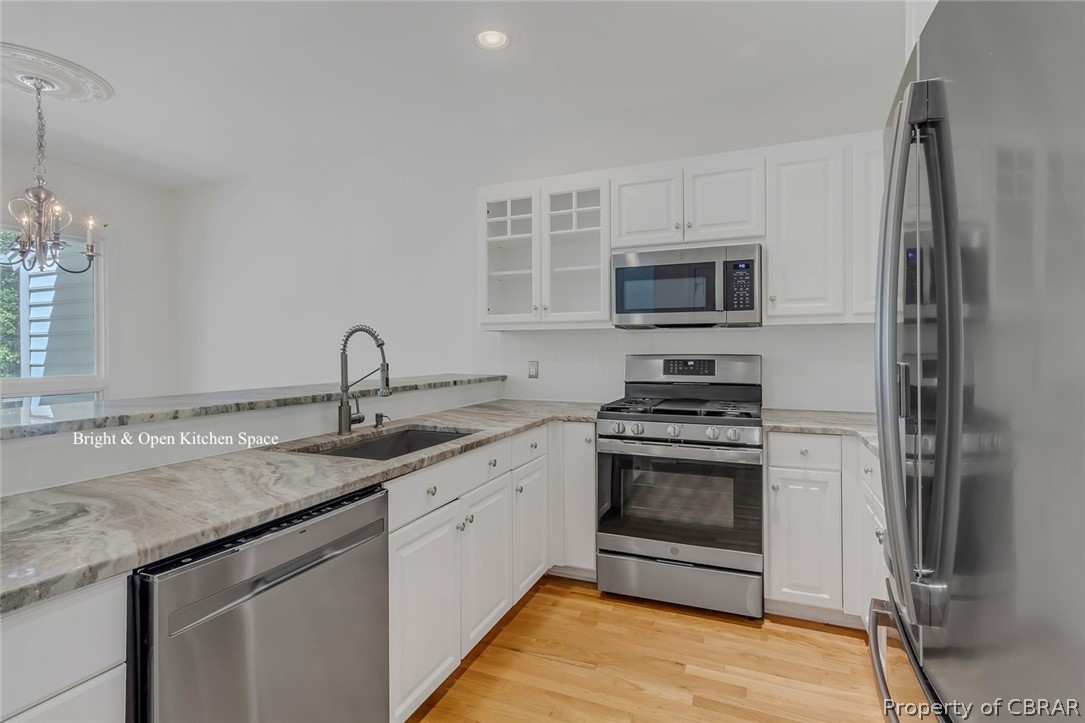 Kitchen featuring appliances with stainless steel finishes, light hardwood / wood-style flooring, white cabinetry, sink, and an inviting chandelier