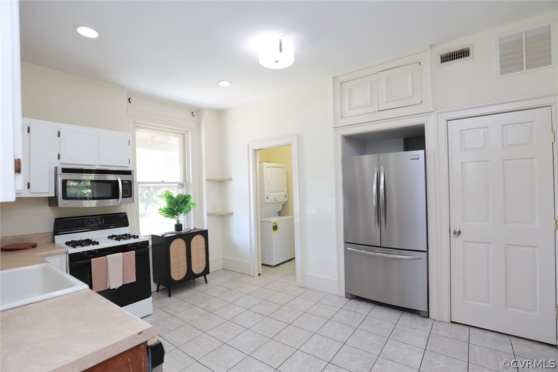 Kitchen featuring stacked washer / dryer, sink, light tile flooring, white cabinetry, and stainless steel appliances