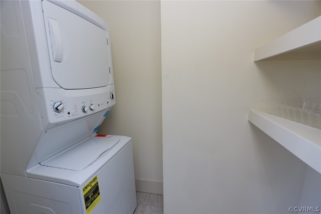 Washroom featuring stacked washer / drying machine and light tile floors