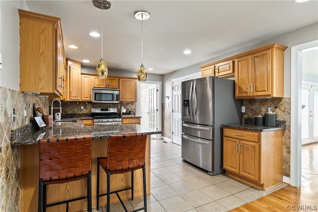 Kitchen with hanging light fixtures, kitchen peninsula, appliances with stainless steel finishes, light tile floors, and tasteful backsplash