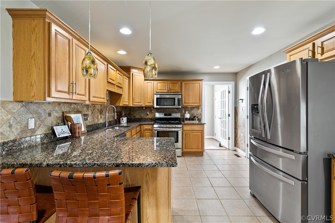 Kitchen with appliances with stainless steel finishes, kitchen peninsula, backsplash, and decorative light fixtures