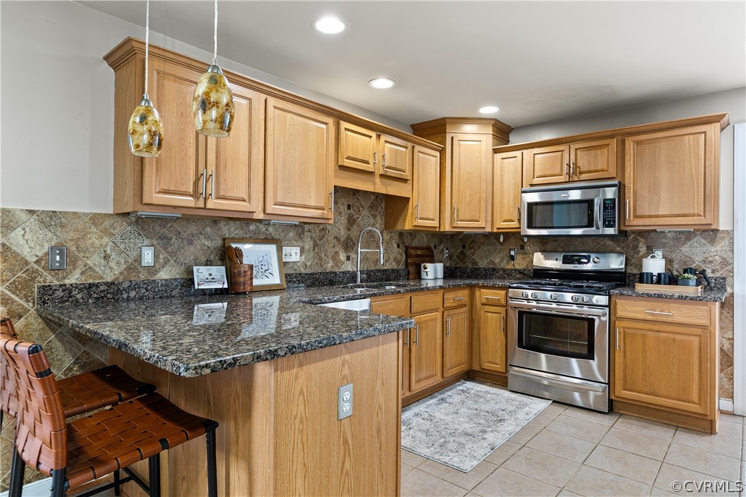 Kitchen with appliances with stainless steel finishes, a breakfast bar area, tasteful backsplash, and light tile flooring