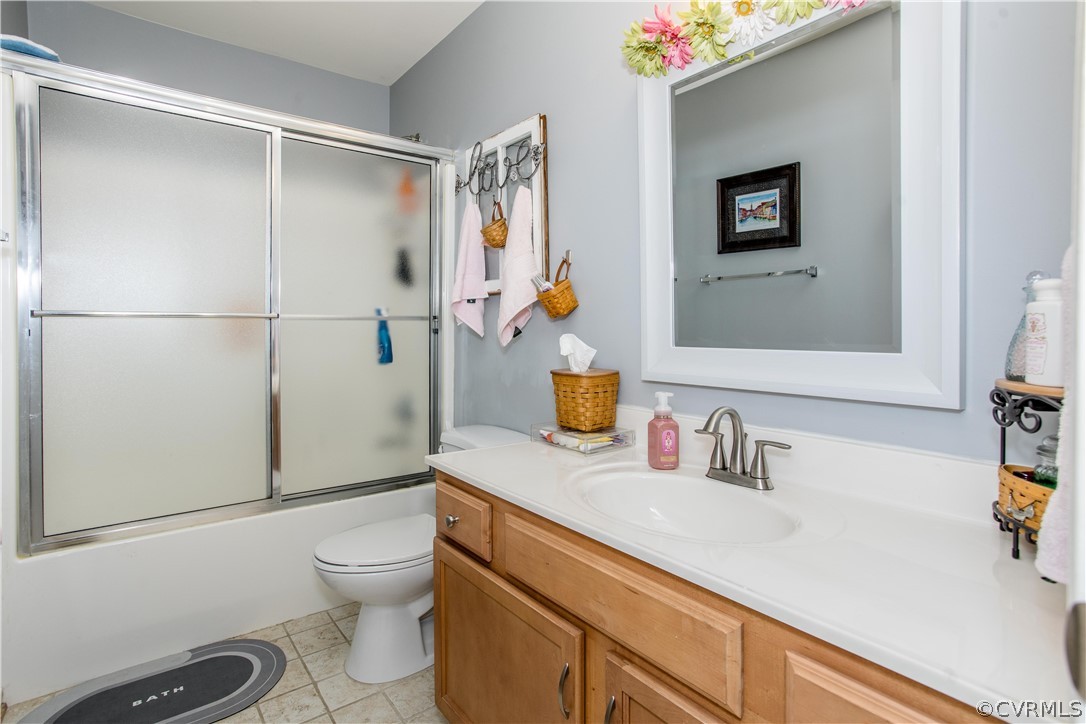Full bathroom featuring toilet, vanity, tile floors, and combined bath / shower with glass door