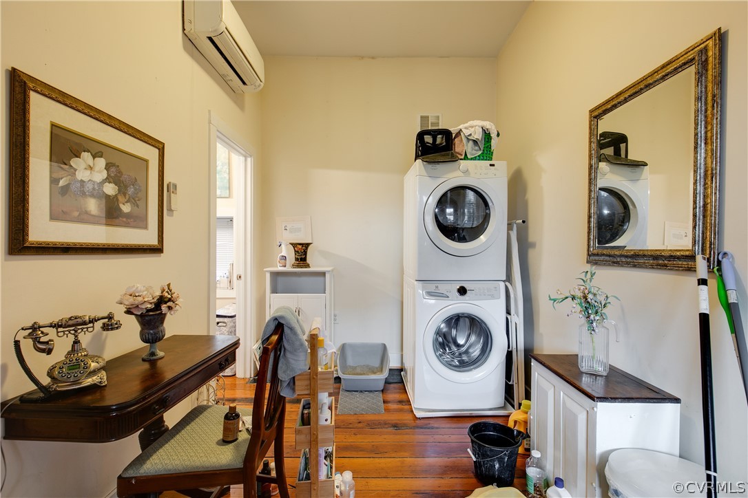 Laundry room with stacked washer and clothes dryer, a wall mounted air conditioner, and dark hardwood / wood-style floors
