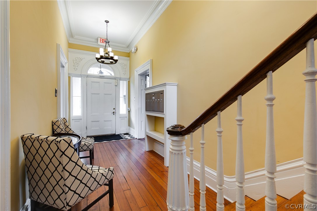 Entrance foyer featuring ornamental molding, an inviting chandelier, and wood-type flooring