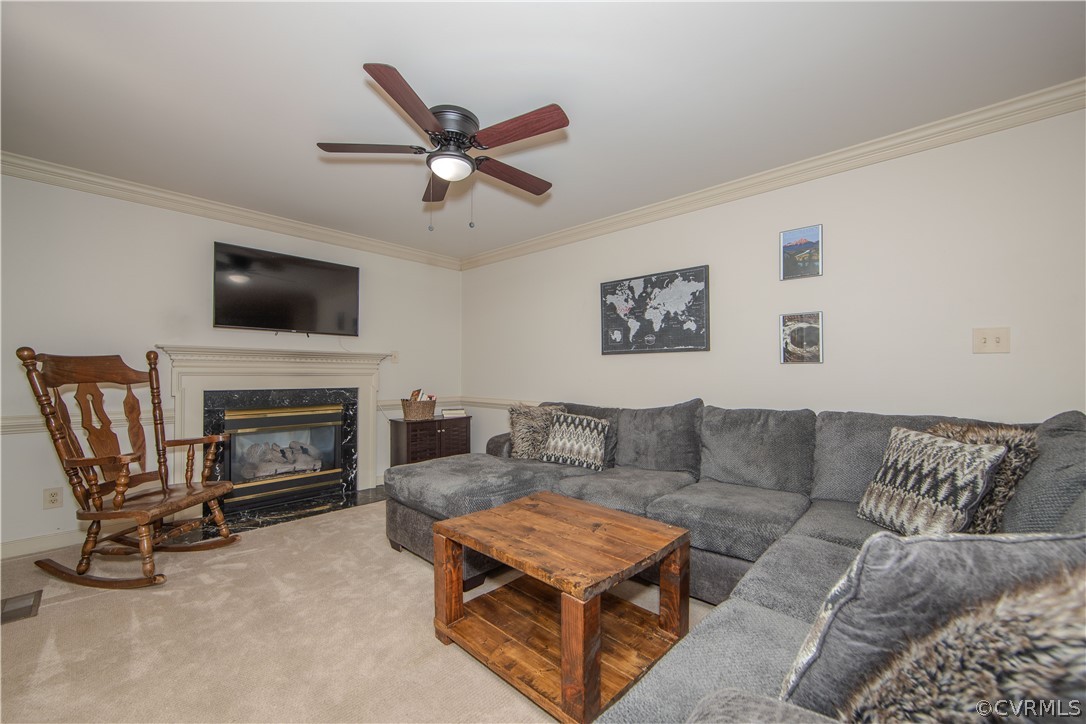 Family room featuring a gas fireplace, ceiling fan, crown molding, and carpeted floors!