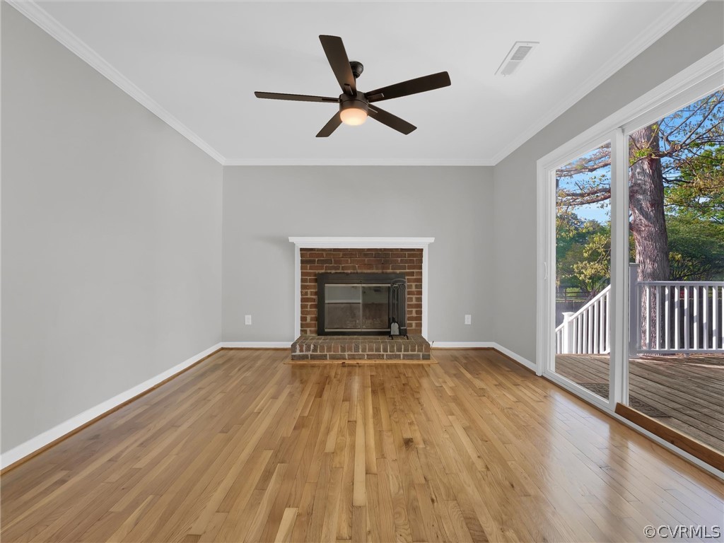 Unfurnished living room with ornamental molding, ceiling fan, light wood-type flooring, and a brick fireplace