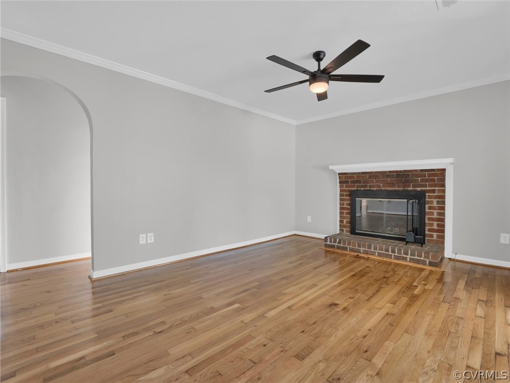 Unfurnished living room with ornamental molding, ceiling fan, a fireplace, and light wood-type flooring
