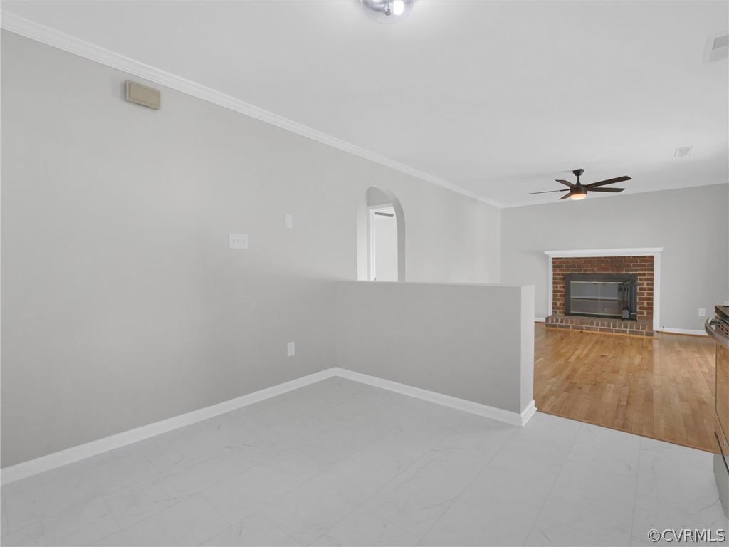 Empty room featuring crown molding, a brick fireplace, ceiling fan, and light tile flooring