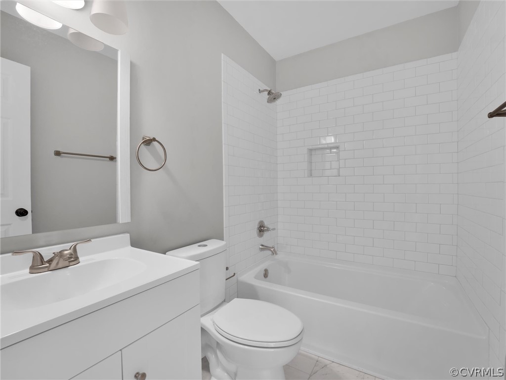 Full bathroom featuring large vanity, tile floors, toilet, and tiled shower / bath