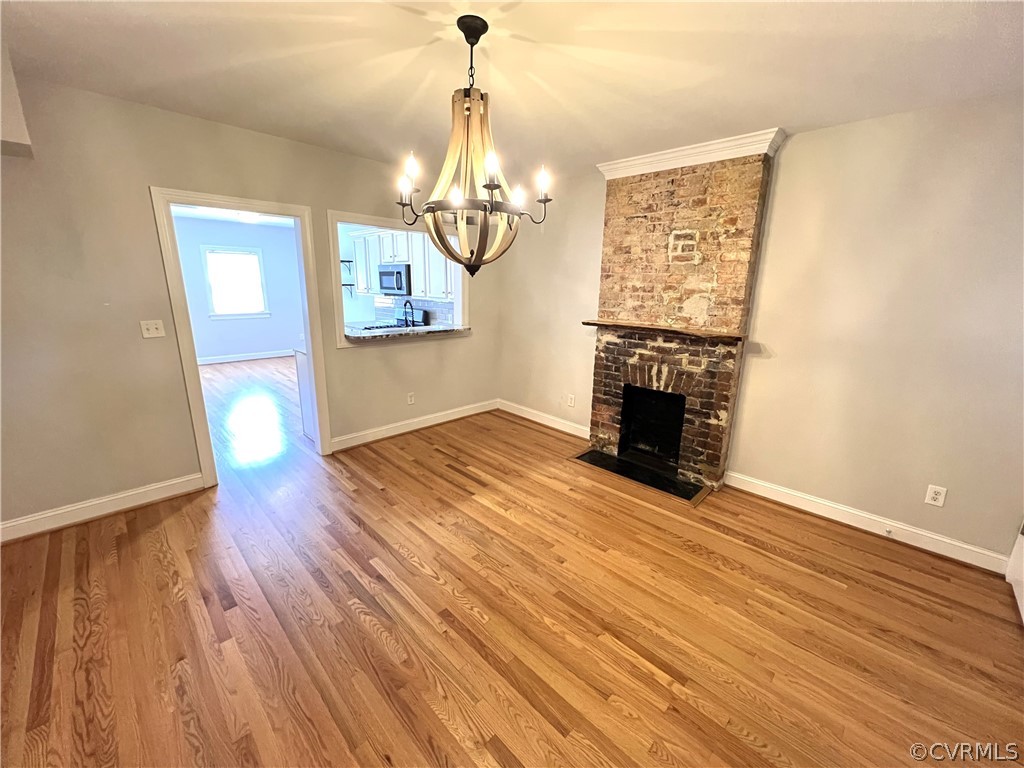 Unfurnished living room featuring hardwood / wood-style flooring, an inviting chandelier, and a brick fireplace