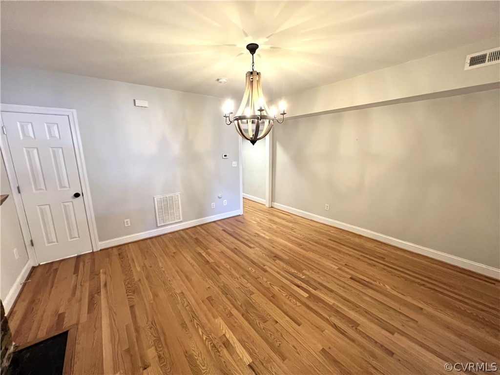 Spare room featuring wood-type flooring and a chandelier