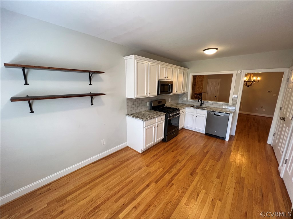 Kitchen with white cabinetry, black appliances, sink, tasteful backsplash, and light hardwood / wood-style floors