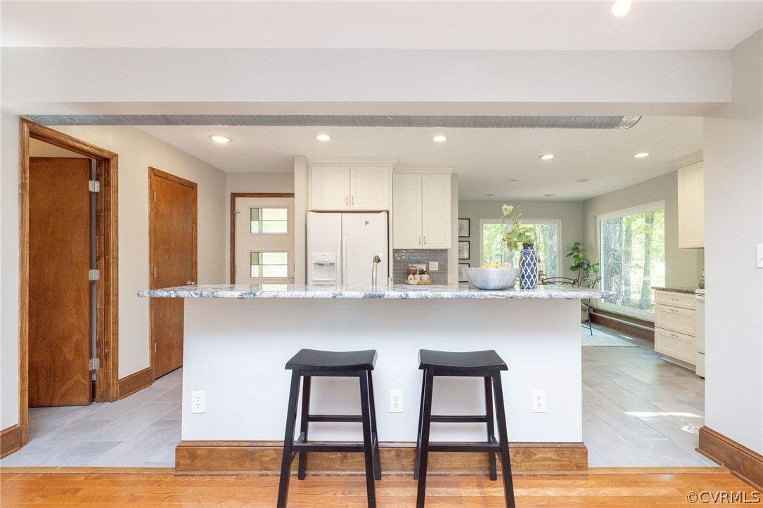 Kitchen featuring tasteful backsplash, white refrigerator with ice dispenser, white cabinetry, and light tile flooring