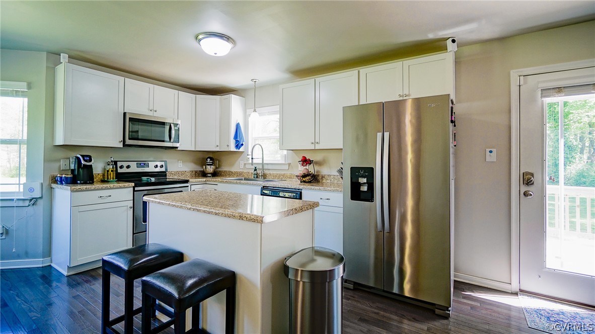 Kitchen featuring decorative light fixtures, appliances with stainless steel finishes, dark wood-type flooring, white cabinetry, and a center island