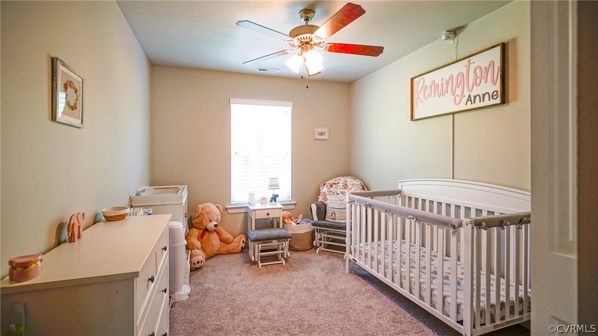 Bedroom with ceiling fan, a crib, and carpet floors