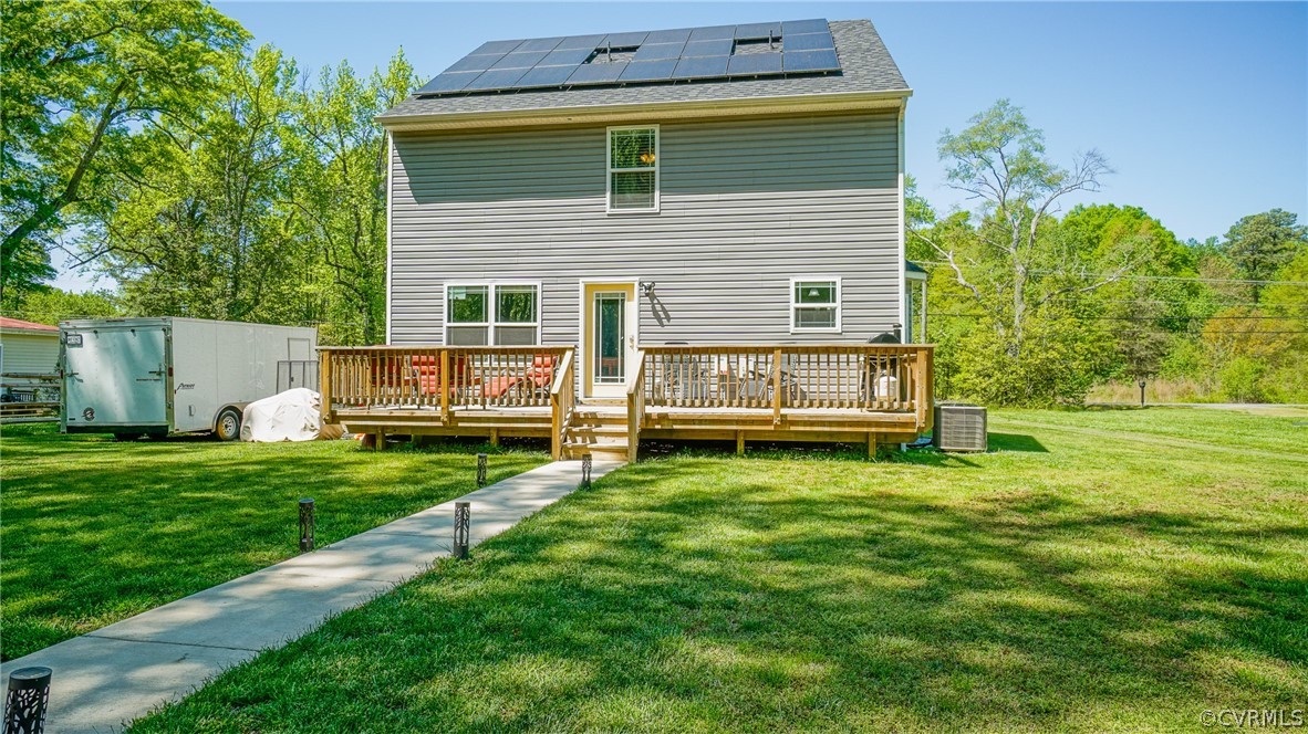 Back of property featuring a deck, a yard, solar panels, and central AC
