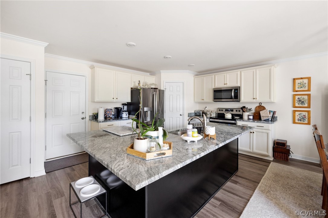 Kitchen with stainless steel appliances, an island with sink, white cabinetry, dark hardwood / wood-style flooring, and a breakfast bar