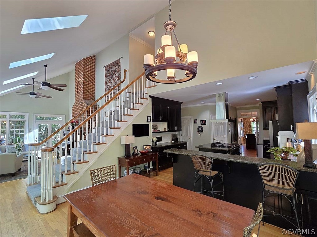 Dining room with brick wall, ceiling fan with notable chandelier, a skylight, light wood-type flooring, and ornamental molding