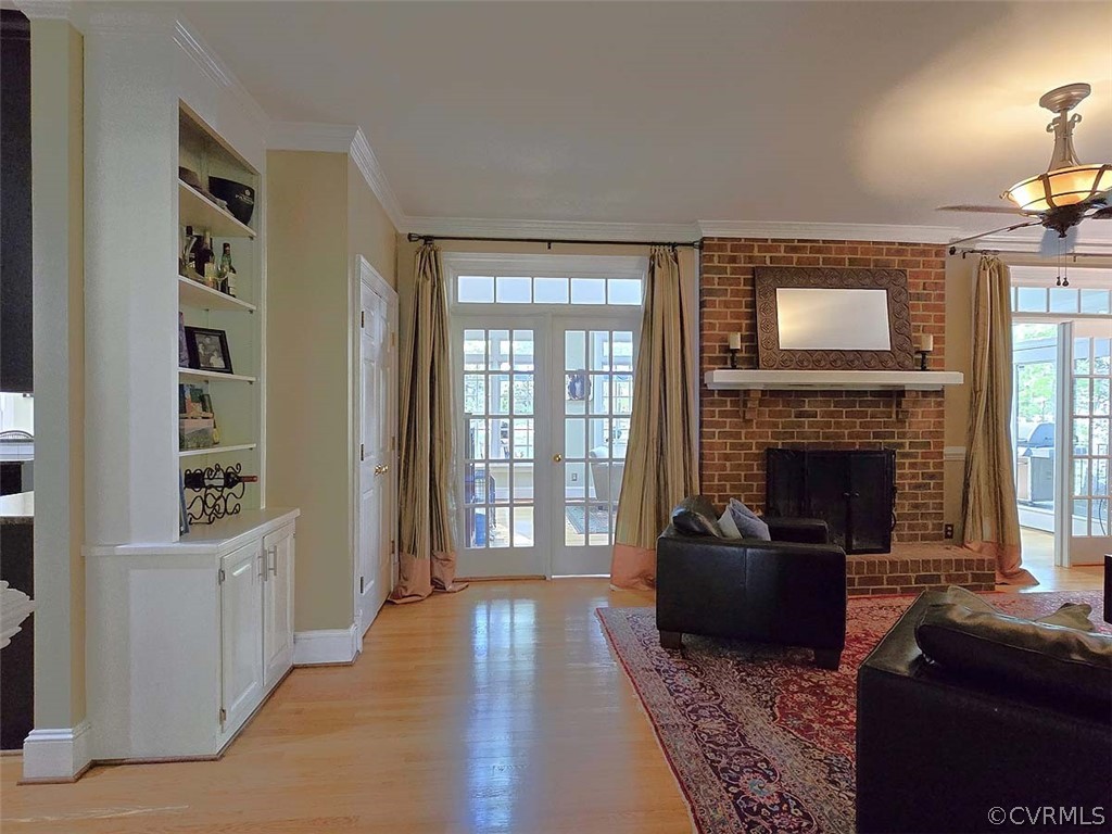 Living room with ornamental molding, a fireplace, light wood-type flooring, brick wall, and built in features