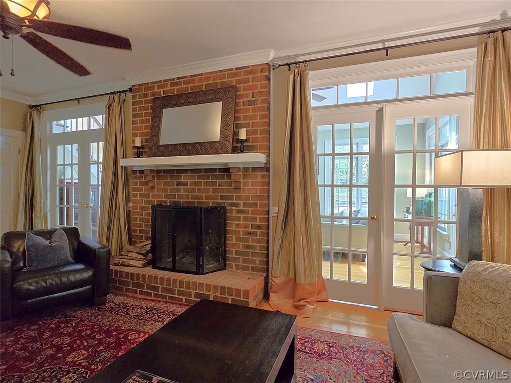 Living room featuring ceiling fan, crown molding, brick wall, wood-type flooring, and a fireplace