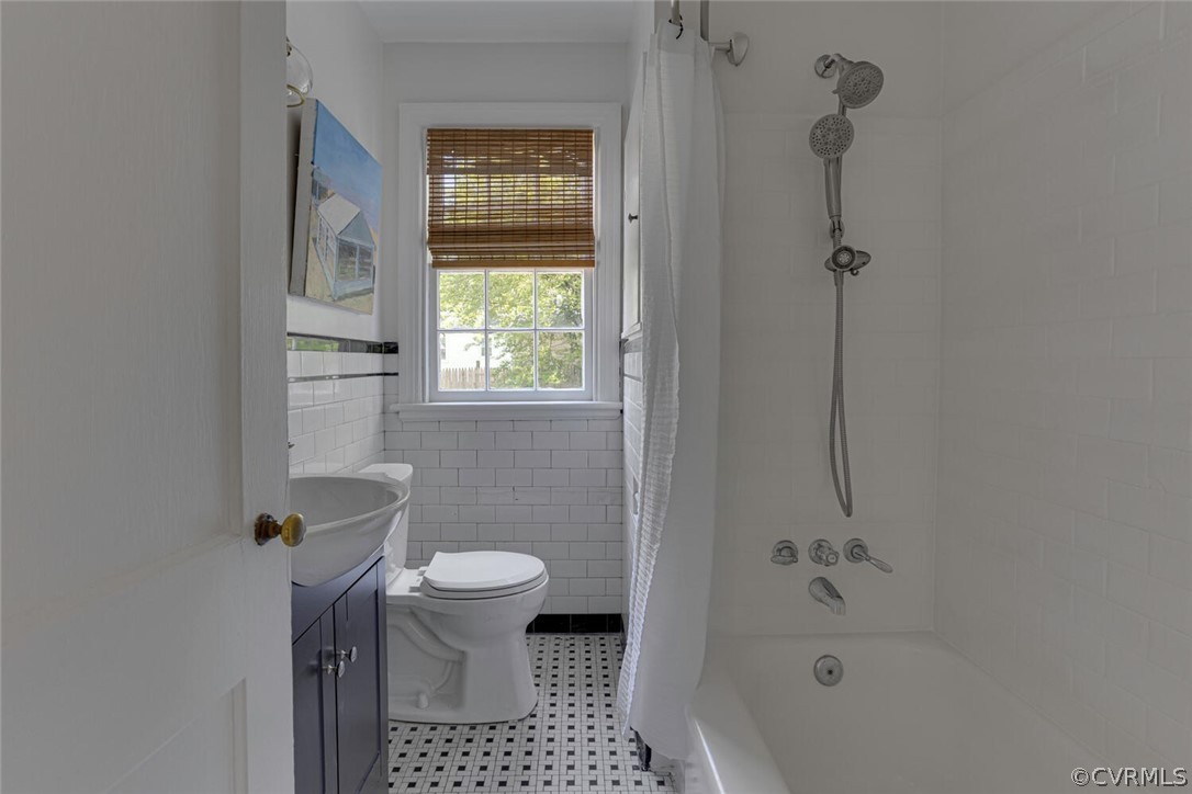 Full bathroom with tile flooring, tile walls, toilet, vanity, and shower / bathtub combination with curtain