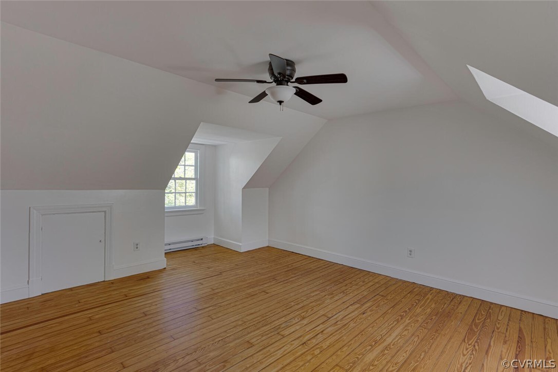 Additional living space featuring a baseboard radiator, ceiling fan, light wood-type flooring, and vaulted ceiling