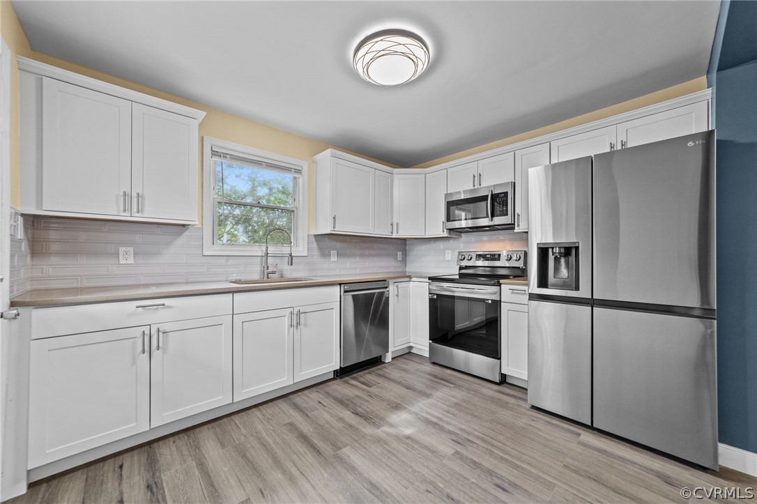 Kitchen with backsplash, stainless steel appliances, sink, and light wood-type flooring
